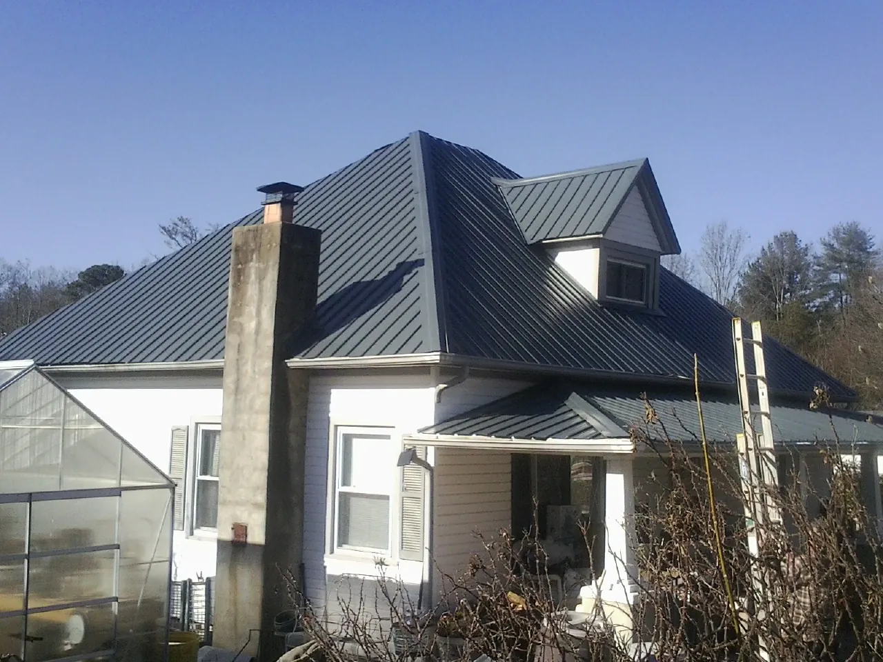 Dark blue standing seam metal roof on a white farmhouse with dormer — Slate & Tile Roof Repair by Roofing Brothers in Plattsburg