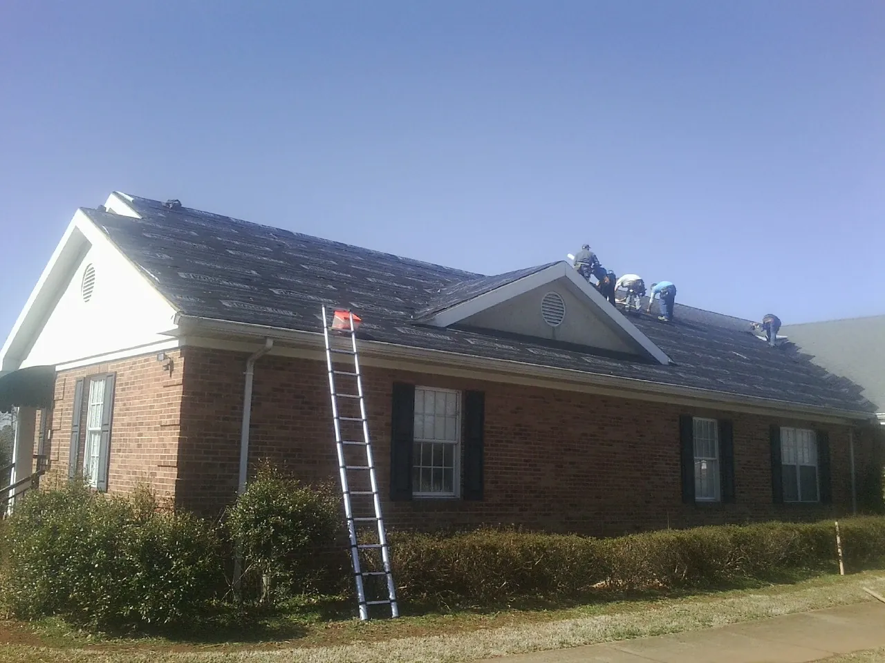 Crew tearing shingles off a brick ranch roof with a ladder set — Emergency Roof Repair work by our crew in Plattsburg
