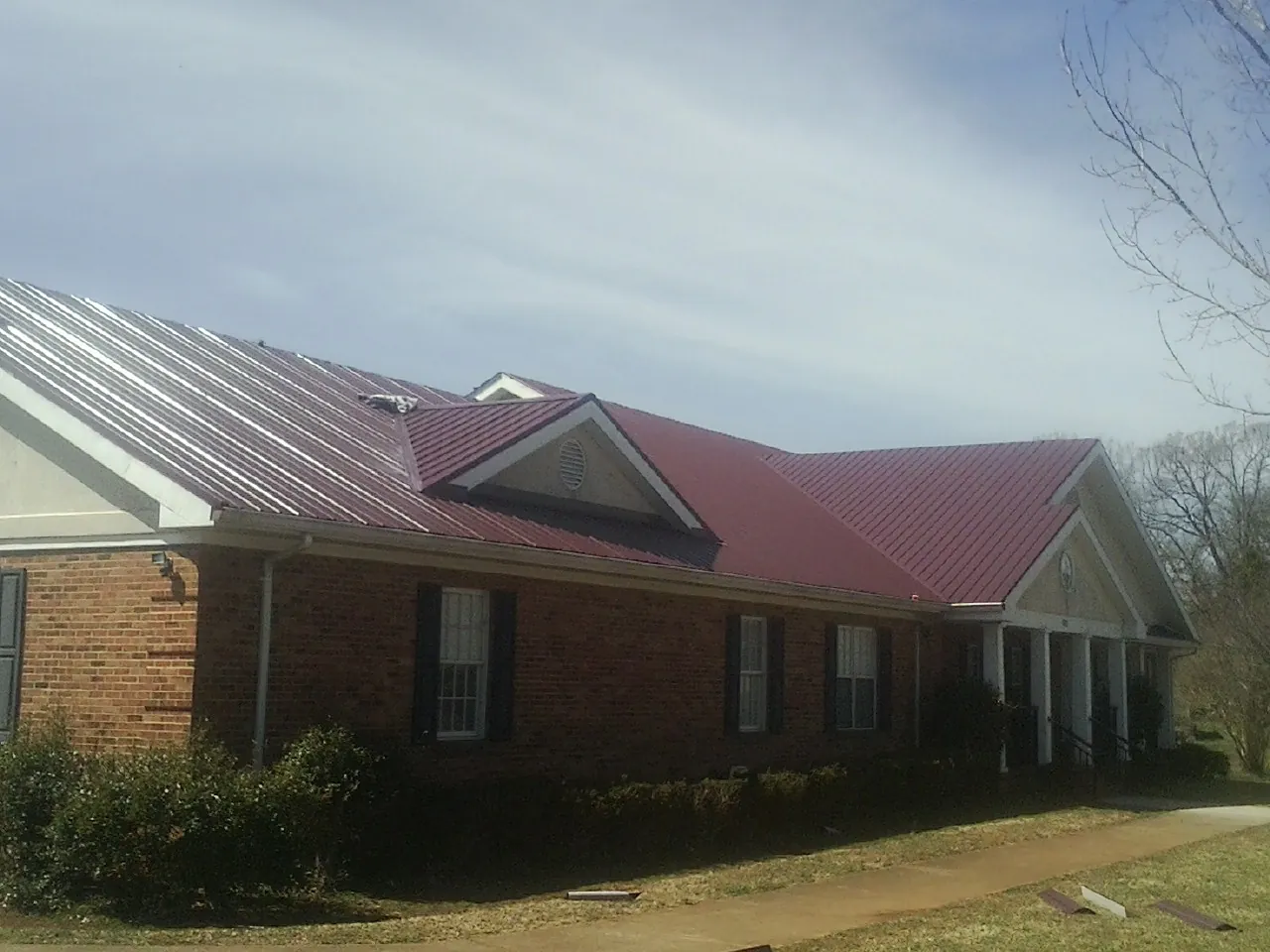 Red metal roof with gabled entries on a long brick building, from a Hail Damage Roof Repair job in Plattsburg