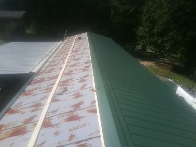 Old rusted panels beside newly installed green metal roofing — Wind Damage Roof Repair by Roofing Brothers in Plattsburg