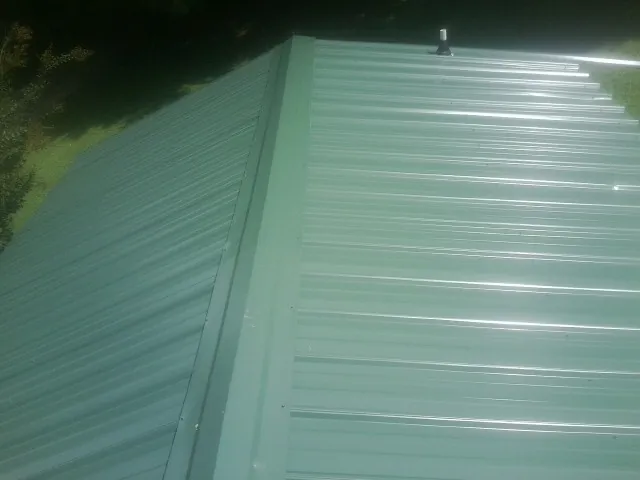 New green metal panels meeting at the ridge of a roof — Flat Roof Repair work by our crew in Plattsburg