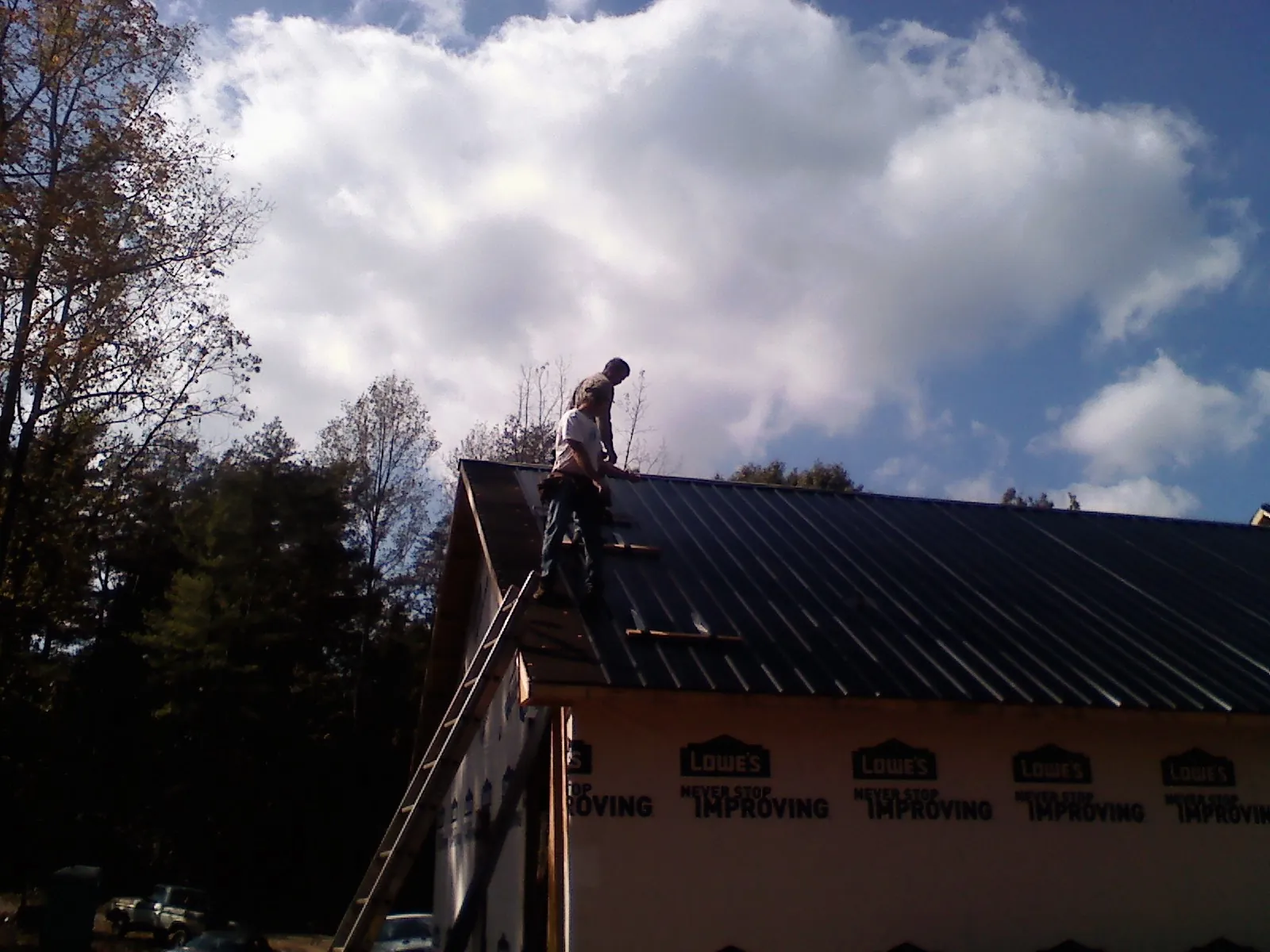 Roofer fastening dark metal panels high against a cloudy sky, from a Roof Inspection job in Plattsburg