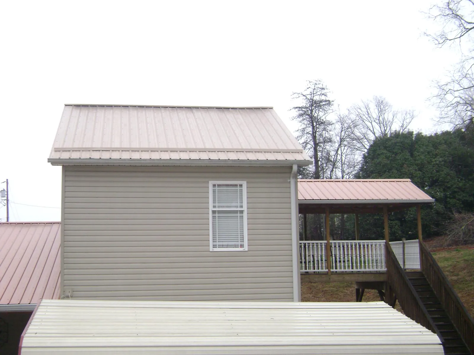 Tan metal roofs on a two story addition and attached porch, from a Roof Replacement job in Plattsburg