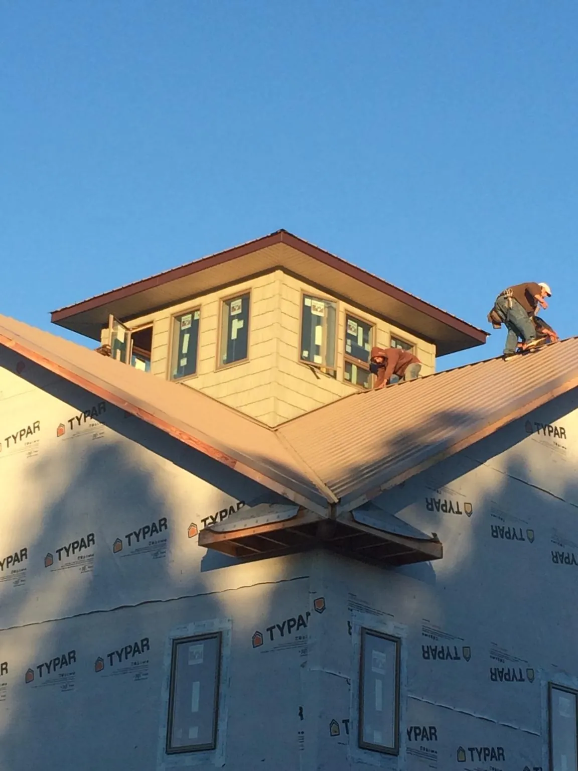 Roofers working around a rooftop cupola on a new metal roof at sunset — Roof Waterproofing in Plattsburg by Roofing Brothers